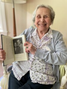 Dorothy poses with a copy of her book, opened on a page of her and her husband.