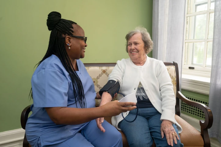 A healthcare staff member takes the blood pressure of a smiling resident